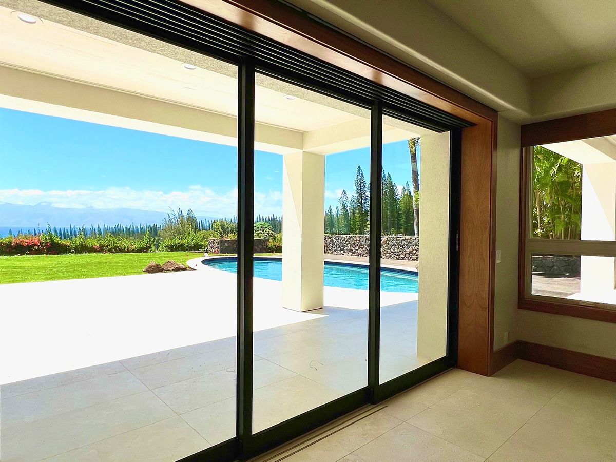 Wide sliding doors opening from a renovated room to a pool and ocean view